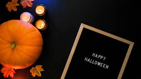 Pumpkin, burning candles, autumn leaves and the inscription Happy Halloween in a wooden frame on a black backgroundの写真素材