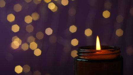 Close-up burning candle in a brown glass with selective focus on golden bokeh backgroundの写真素材
