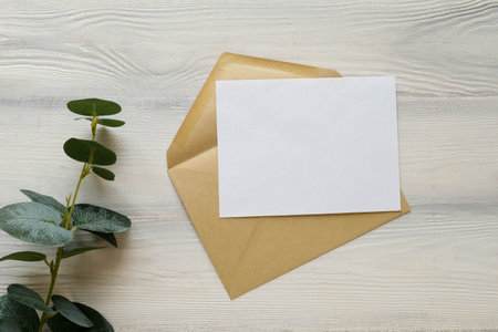 Postal envelope and a blank sheet on a light wooden background. Green plant branches and a letter with space for textの写真素材