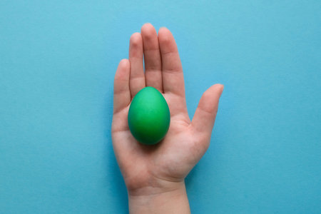 Colored Easter egg in a hand on a blue backgroundの写真素材