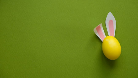 Easter rabbit ears on a yellow egg on a green background with a place for textの写真素材