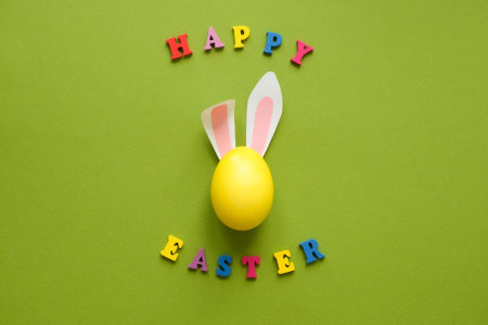 Easter rabbit ears on a yellow egg and text Happy Easter on a green backgroundの写真素材