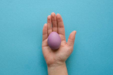 Colored purple Easter egg in a hand on a blue backgroundの写真素材