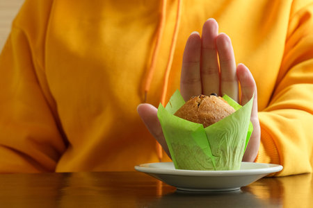 No sweets - a woman in a yellow hoodie is gesturing no to a muffin. Refusal of sugar. Diet and healthy eatingの写真素材
