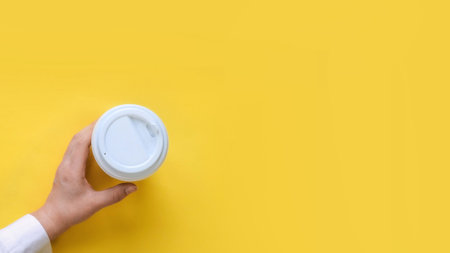 Hand take a glass of coffee to go with white plastic lid top view on yellow backgroundの写真素材