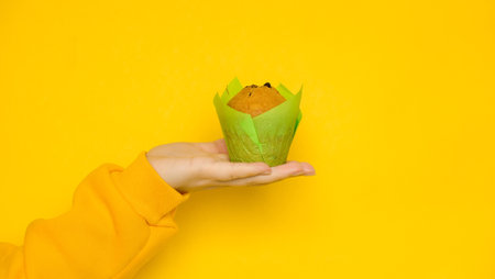 Female hand with a muffin on a yellow background with a place for a textの写真素材