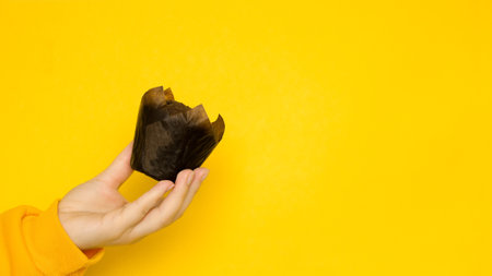Female hand with a chocolate muffin on a yellow background with a place for a textの写真素材