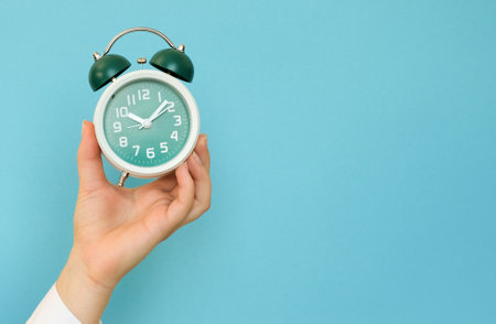 Hand holding a classic alarm clock on a blue background