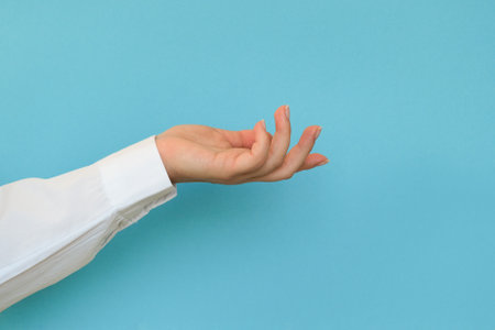 A hand in a white shirt holds something on a blue background