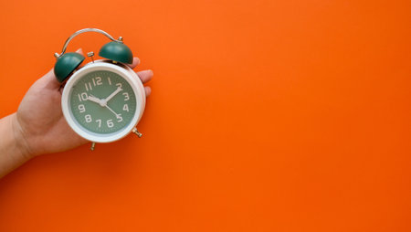 Hand holds classic green alarm clock on orange background with a copy spaceの写真素材