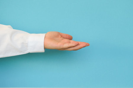 A hand in a white shirt holds something on a blue backgroundの写真素材