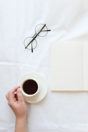 Opened note and hand with a coffee cup on a white sheet. Cozy composition on a bed