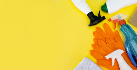 Cleaning bottles, rag, sponge and orange rubber gloves - flatlay with place for text on yellow...