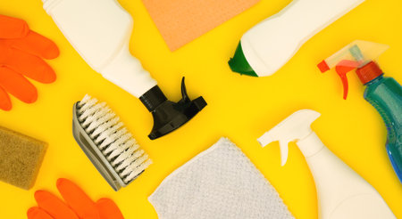 Cleaning bottles, rag, sponge, brush and orange rubber gloves on yellow background