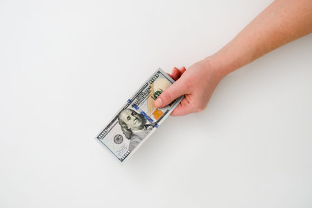 A woman's hand holds one hundred-dollar bill on a white background