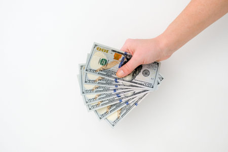 A woman's hand holds a few hundred-dollar bill on a white background