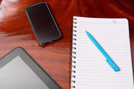 Tablet with notebook on wooden table and penの写真素材