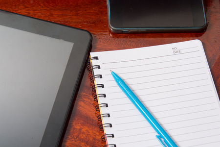 Tablet with notebook on wooden table and penの写真素材