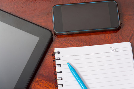 Tablet with notebook on wooden table and penの写真素材