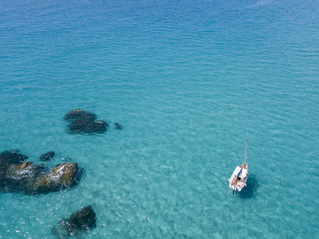 Aerial view of a moored boat floating on a transparent sea. Diving relaxation and summer vacations. Italian coasts, beaches and rocksの写真素材