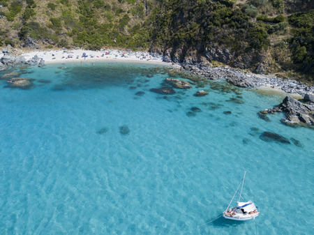 Aerial view of a moored boat floating on a transparent sea. Beach with promontory overlooking the sea. Zambrone, Calabria, Italy. Diving relaxation and summer vacations. Italian coasts, beaches and rocksの写真素材