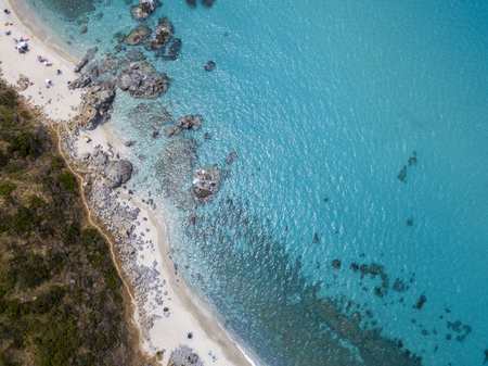 Aerial view of the rocks on the sea. Overview of seabed seen from above, transparent water. Swimmers, bathers floating on the waterの写真素材