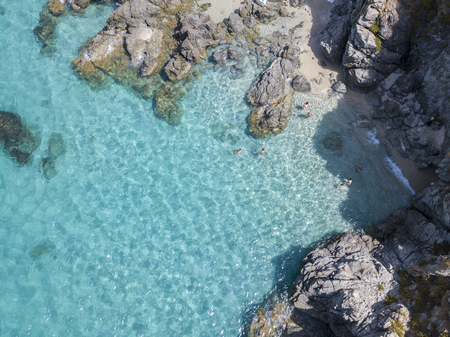 Aerial view of the rocks on the sea. Overview of seabed seen from above, transparent water. Swimmers, bathers floating on the waterの写真素材