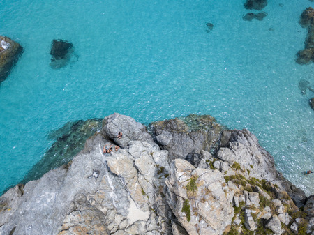 Aerial view of the rocks on the sea. Overview of seabed seen from above, transparent water. Swimmers, bathers floating on the waterの写真素材