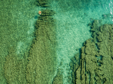Aerial view of a canoe in the water floating on a transparent sea. Bathers at sea. Zambrone, Calabria, Italy. Diving relaxation and summer vacations. Italian coasts, beaches and rocks.の写真素材