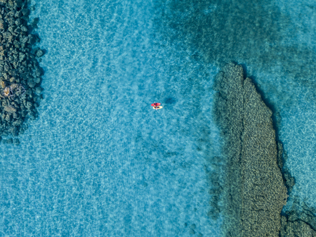 Aerial view of a canoe in the water floating on a transparent sea. Bathers at sea. Zambrone, Calabria, Italy. Diving relaxation and summer vacations. Italian coasts, beaches and rocks.の写真素材