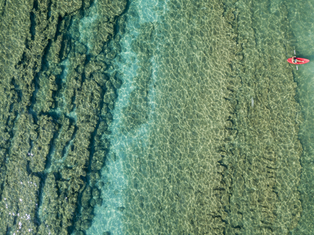 Aerial view of a canoe in the water floating on a transparent sea. Bathers at sea. Zambrone, Calabria, Italy. Diving relaxation and summer vacations. Italian coasts, beaches and rocks.の写真素材