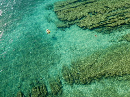 Aerial view of a canoe in the water floating on a transparent sea. Bathers at sea. Zambrone, Calabria, Italy. Diving relaxation and summer vacations. Italian coasts, beaches and rocks.の写真素材