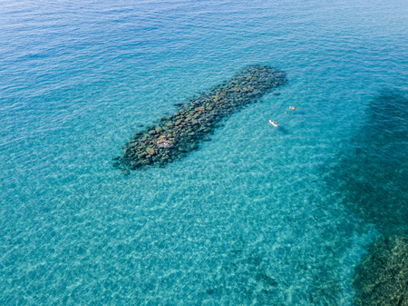 Aerial view of a canoe in the water floating on a transparent sea. Bathers at sea. Zambrone, Calabria, Italy. Diving relaxation and summer vacations. Italian coasts, beaches and rocks.の写真素材