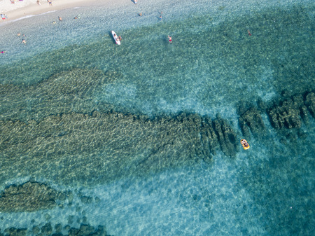 Aerial view of a canoe in the water floating on a transparent sea. Bathers at sea. Zambrone, Calabria, Italy. Diving relaxation and summer vacations. Italian coasts, beaches and rocks.の写真素材