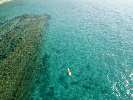 Aerial view of a canoe in the water floating on a transparent sea. Bathers at sea. Zambrone, Calabria, Italy. Diving relaxation and summer vacations. Italian coasts, beaches and rocksの写真素材