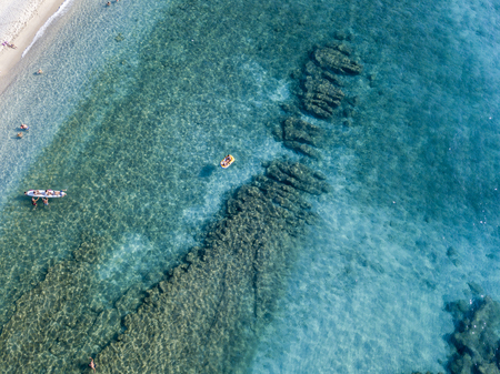 Aerial view of a canoe in the water floating on a transparent sea. Bathers at sea. Zambrone, Calabria, Italy. Diving relaxation and summer vacations. Italian coasts, beaches and rocks.の写真素材
