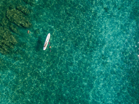 Aerial view of a canoe in the water floating on a transparent sea. Bathers at sea. Zambrone, Calabria, Italy. Diving relaxation and summer vacations. Italian coasts, beaches and rocks.の写真素材
