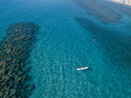 Aerial view of a canoe in the water floating on a transparent sea. Bathers at sea. Zambrone, Calabria, Italy. Diving relaxation and summer vacations. Italian coasts, beaches and rocks.の写真素材