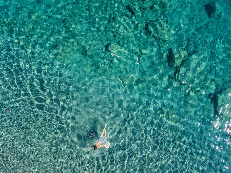 Aerial view of the rocks on the sea. Overview of seabed seen from above, transparent water. Swimmers, bathers floating on the waterの写真素材