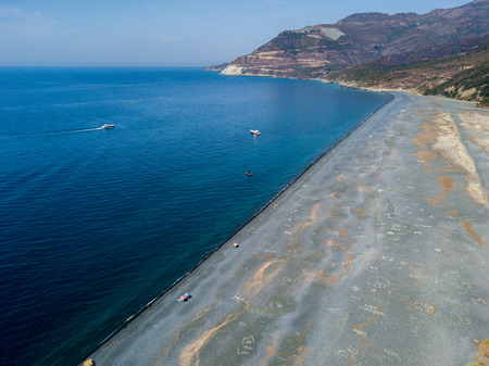 Aerial view of the black pebble beach, Nonza, Geometric designs made with stones, sailboats and moored boats near the beach. Cap Corse Peninsula, Corsica. Coastline. franceの写真素材