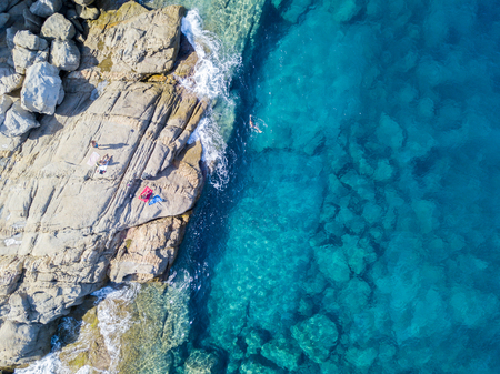 Aerial view of the rocks on the sea. Overview of seabed seen from above, transparent water. Swimmers, bathers floating on the waterの写真素材
