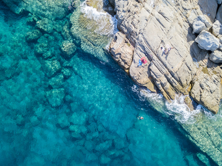 Aerial view of the rocks on the sea. Overview of seabed seen from above, transparent water. Swimmers, bathers floating on the waterの写真素材