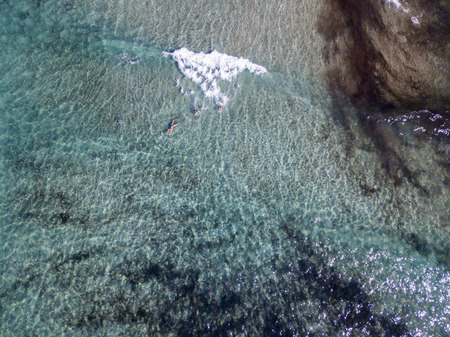 Aerial view of the rocks on the sea. Overview of seabed seen from above, transparent water. Swimmers, bathers floating on the waterの写真素材