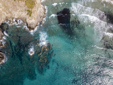 Aerial view of the rocks on the sea. Overview of seabed seen from above, transparent water. Swimmers, bathers floating on the waterの写真素材