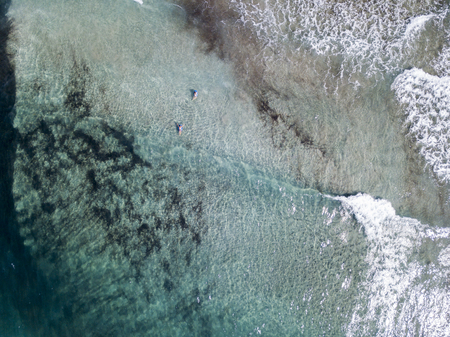 Aerial view of the rocks on the sea. Overview of seabed seen from above, transparent water. Swimmers, bathers floating on the waterの写真素材