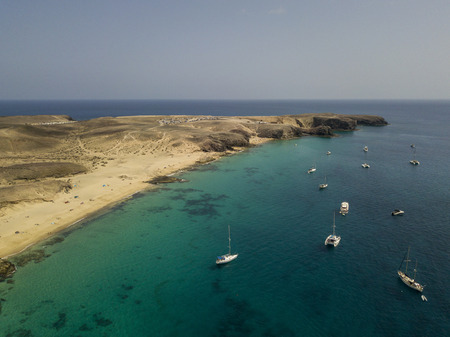 Aerial view of the jagged shores and beaches of Lanzarote, Spain, Canary. Roads and dirt paths. Walking routes to explore the island. Bathers on the beach and in the Atlantic Ocean. Papagayoの写真素材