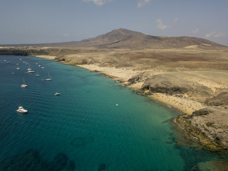 Aerial view of the jagged shores and beaches of Lanzarote, Spain, Canary. Roads and dirt paths. Walking routes to explore the island. Bathers on the beach and in the Atlantic Ocean. Papagayoの写真素材
