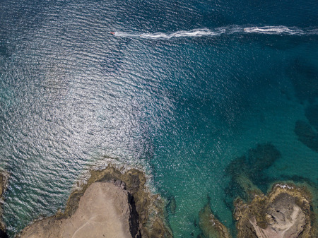 Aerial view of the jagged shores and beaches of Lanzarote, Spain, Canary. Red dinghy navigates at...