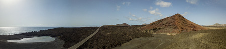 Aerial view of the Bermeja mountain, surrounded by lava fields. Coastal road flowing through black...