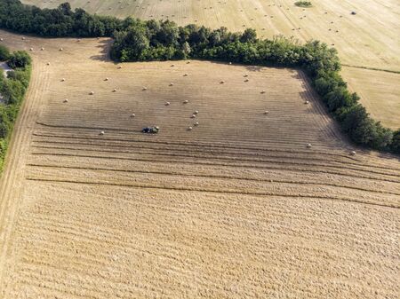 Nature and landscape, aerial view of fields with tractor and harvesting and pressing hay. Field with swaths ready to be transformed into round balesの写真素材